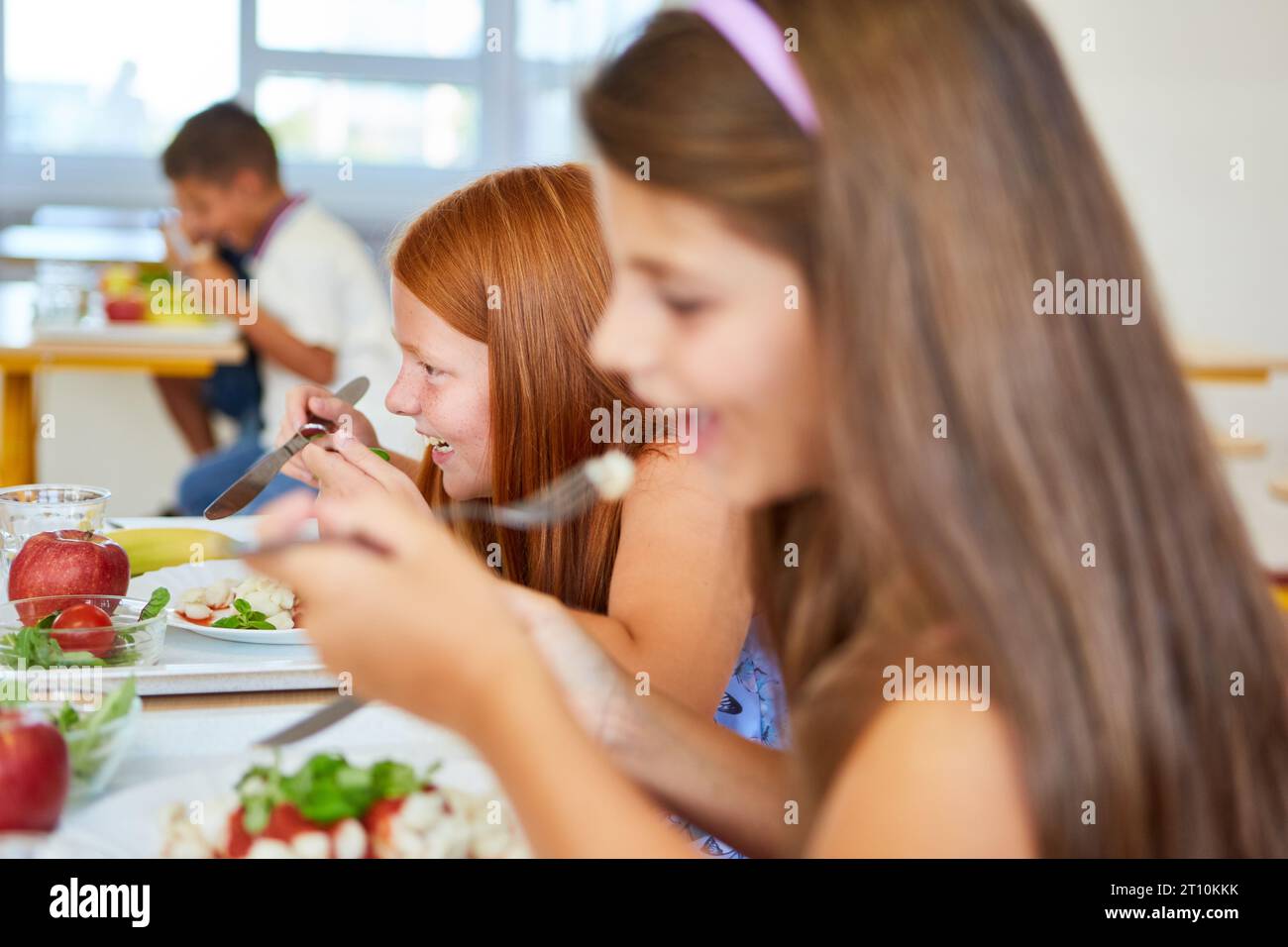 Happy girl having meal with friend during lunch time in school
