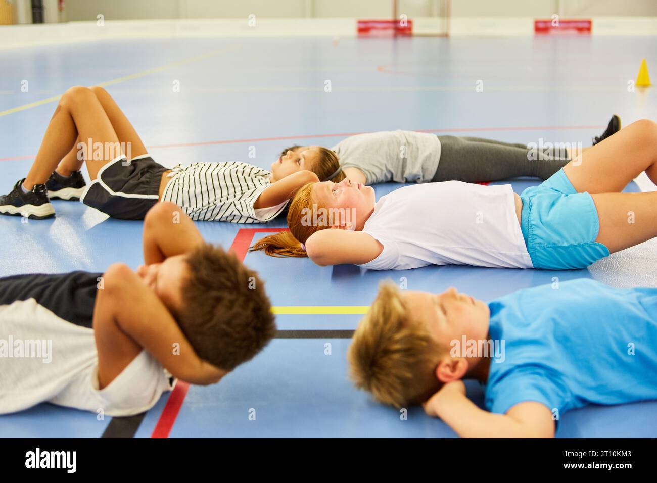 Male and female students exercising while lying down on floor in gym class Stock Photo