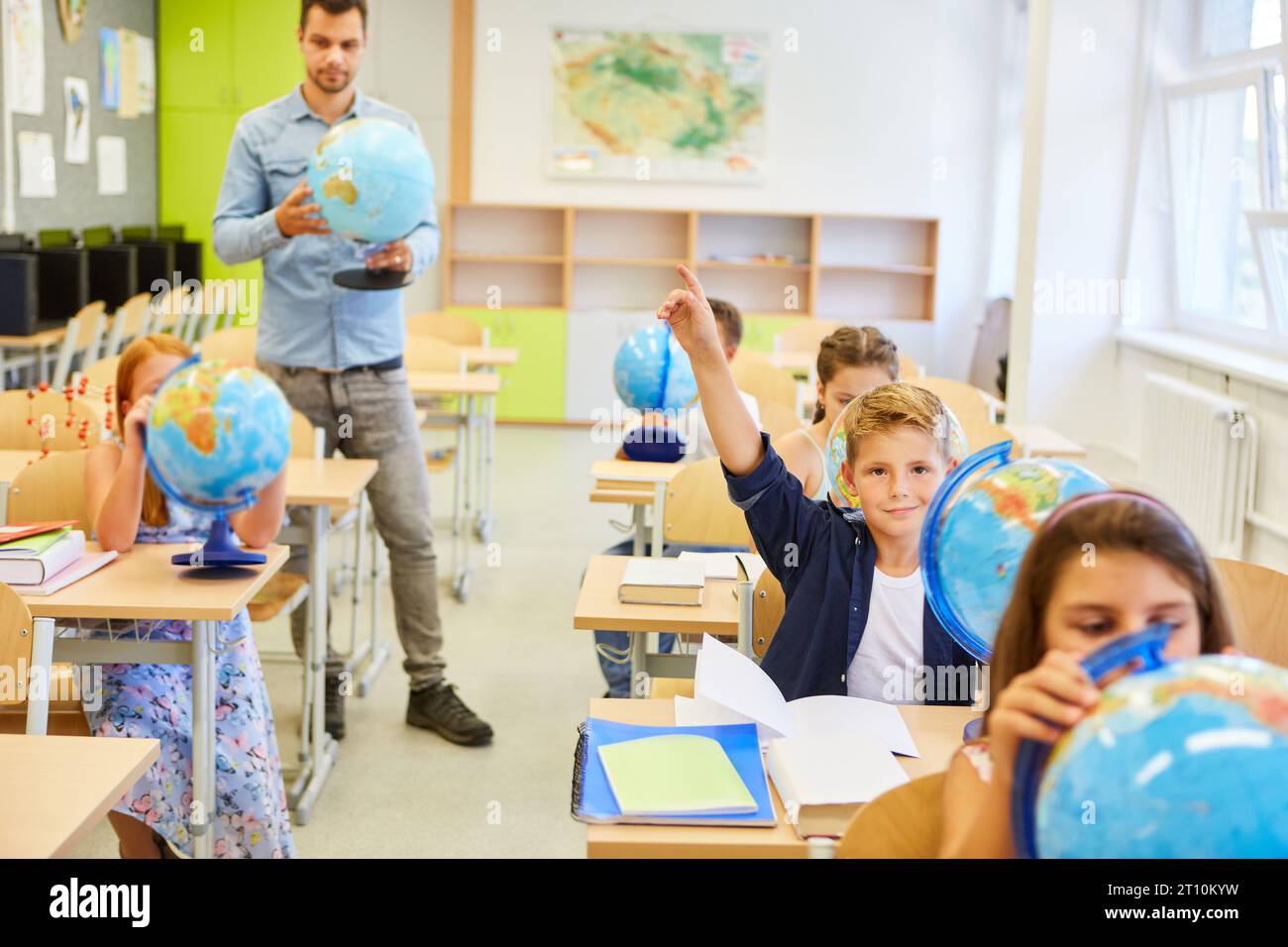 Male and female students studying with globes with teacher in classroom Stock Photo