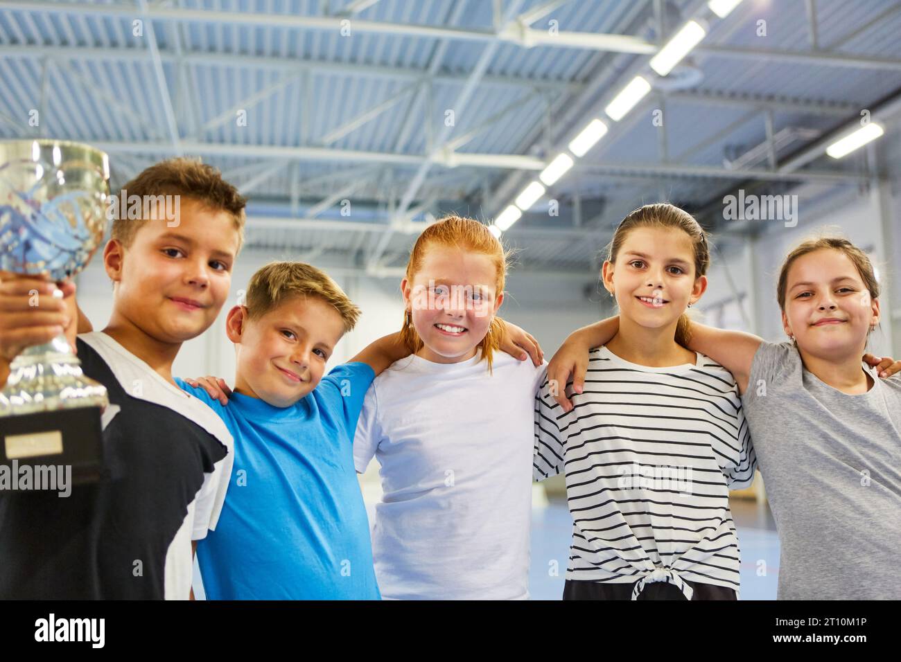 Portrait of smiling male and female students holding trophy while standing in school gym Stock Photo