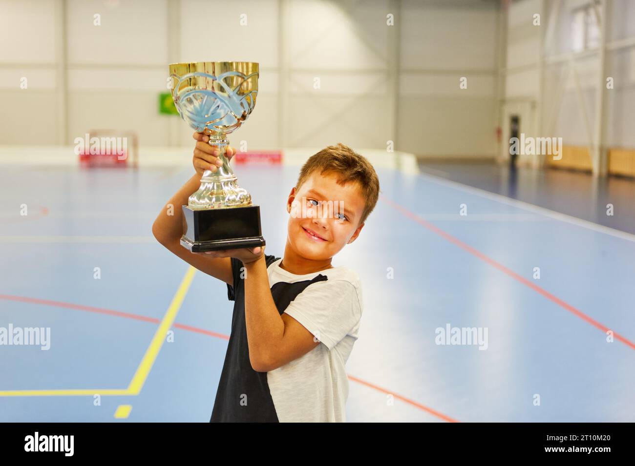 Portrait of smiling schoolboy holding trophy while standing in school gym Stock Photo
