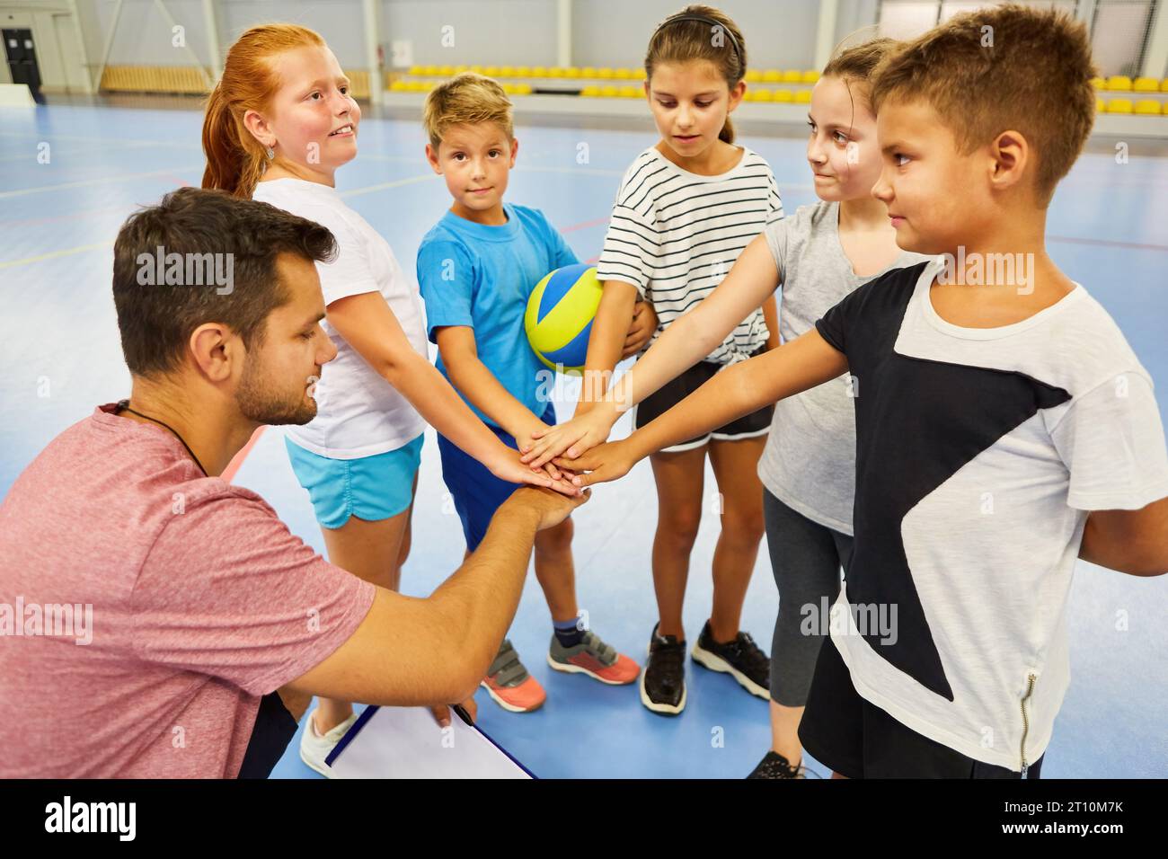 Male and female students stacking hands with teacher during gym class Stock Photo