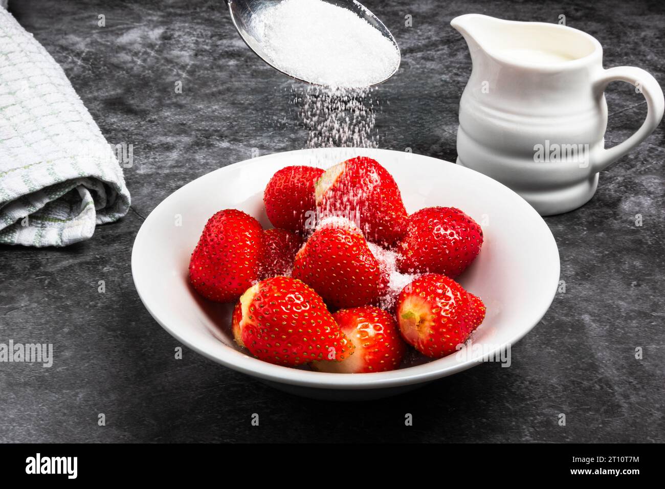pouring sugar on a bowl of strawberries Stock Photo