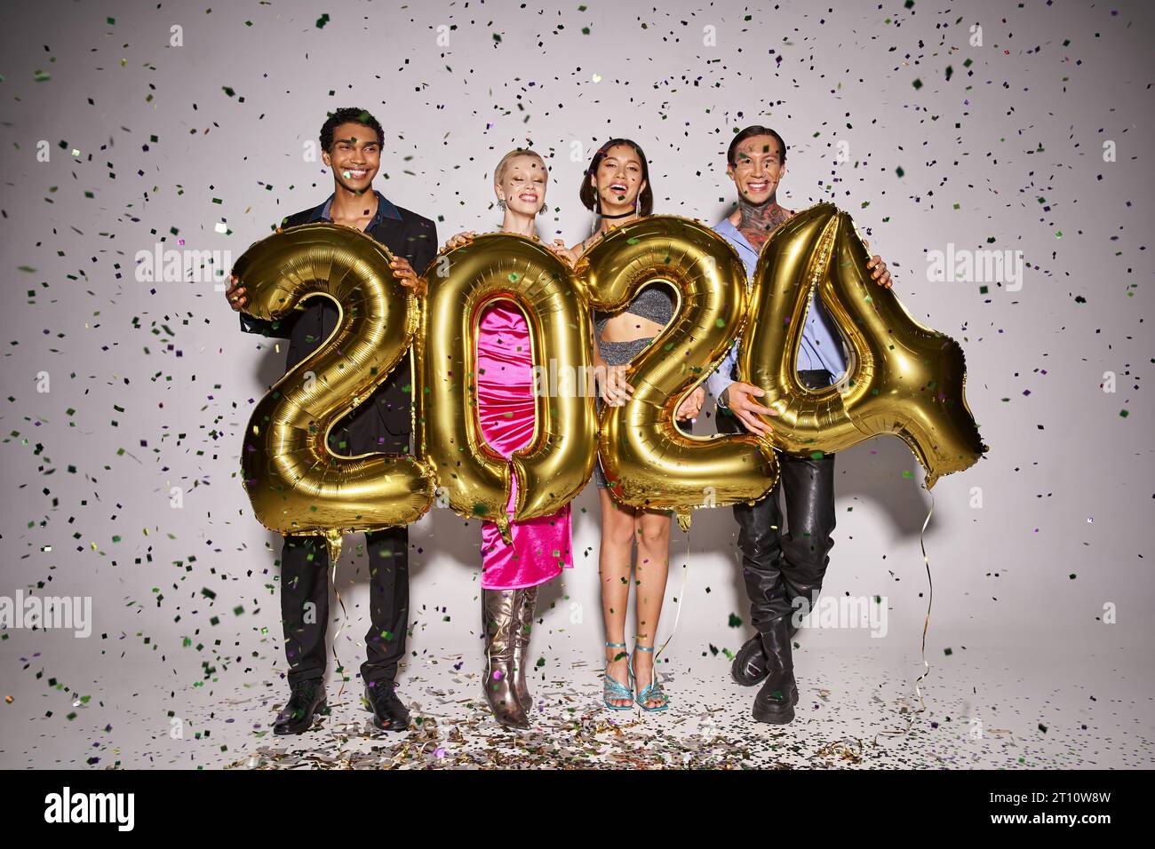 happy interracial friends holding balloons with 2024 numbers near falling confetti, New Year party Stock Photo