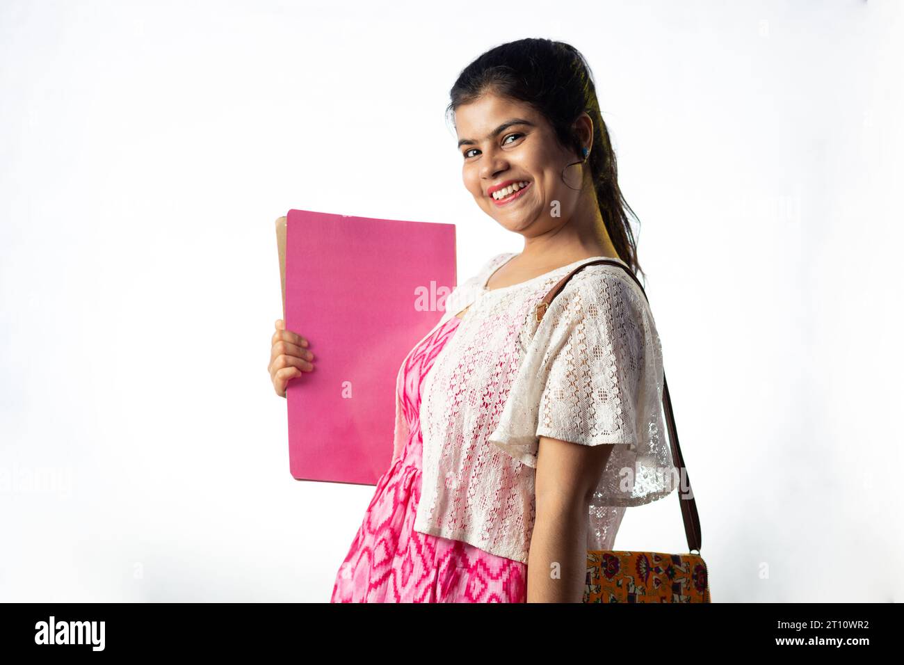 A pretty young Indian girl with books in hand standing with smiling ...