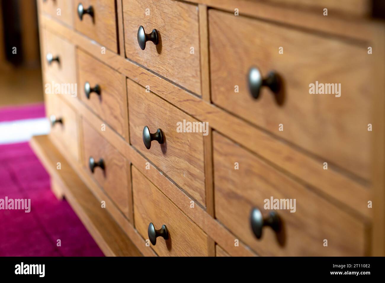 Cabinet of small drawers all closed. Wooden drawers with metal pull knobs. Selective focus on the second row of drawers. Storage in neat compartments Stock Photo