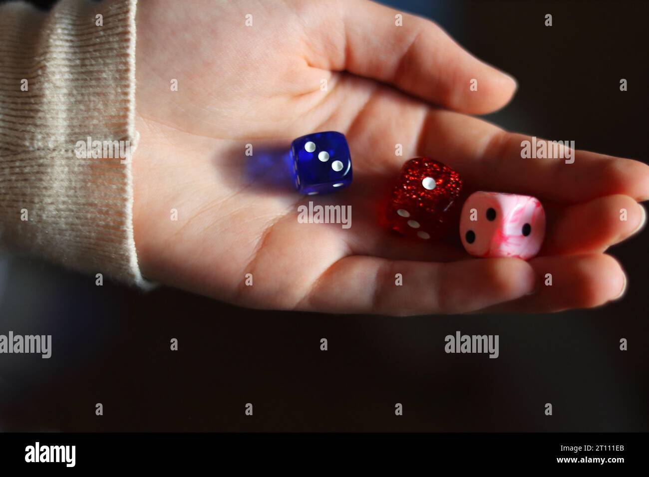 Holding gambling dices. Throwing three Six-seided dice in female's hand. Teenager is rolling three dice. Dark background. Selective focus. Blurred. Stock Photo