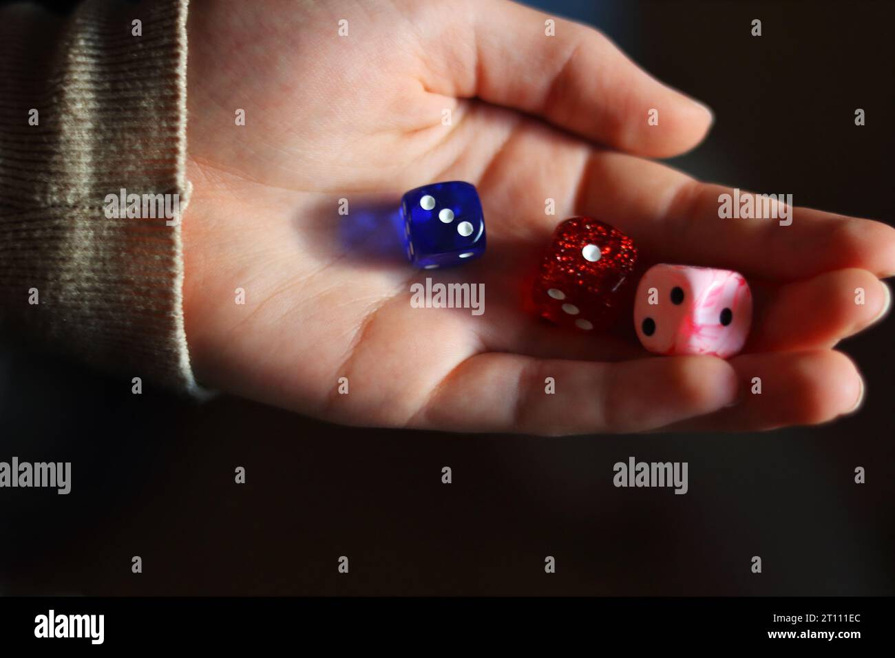Holding gambling dices. Throwing three Six-seided dice in female's hand. Teenager is rolling three dice. Dark background. Selective focus. Blurred. Stock Photo