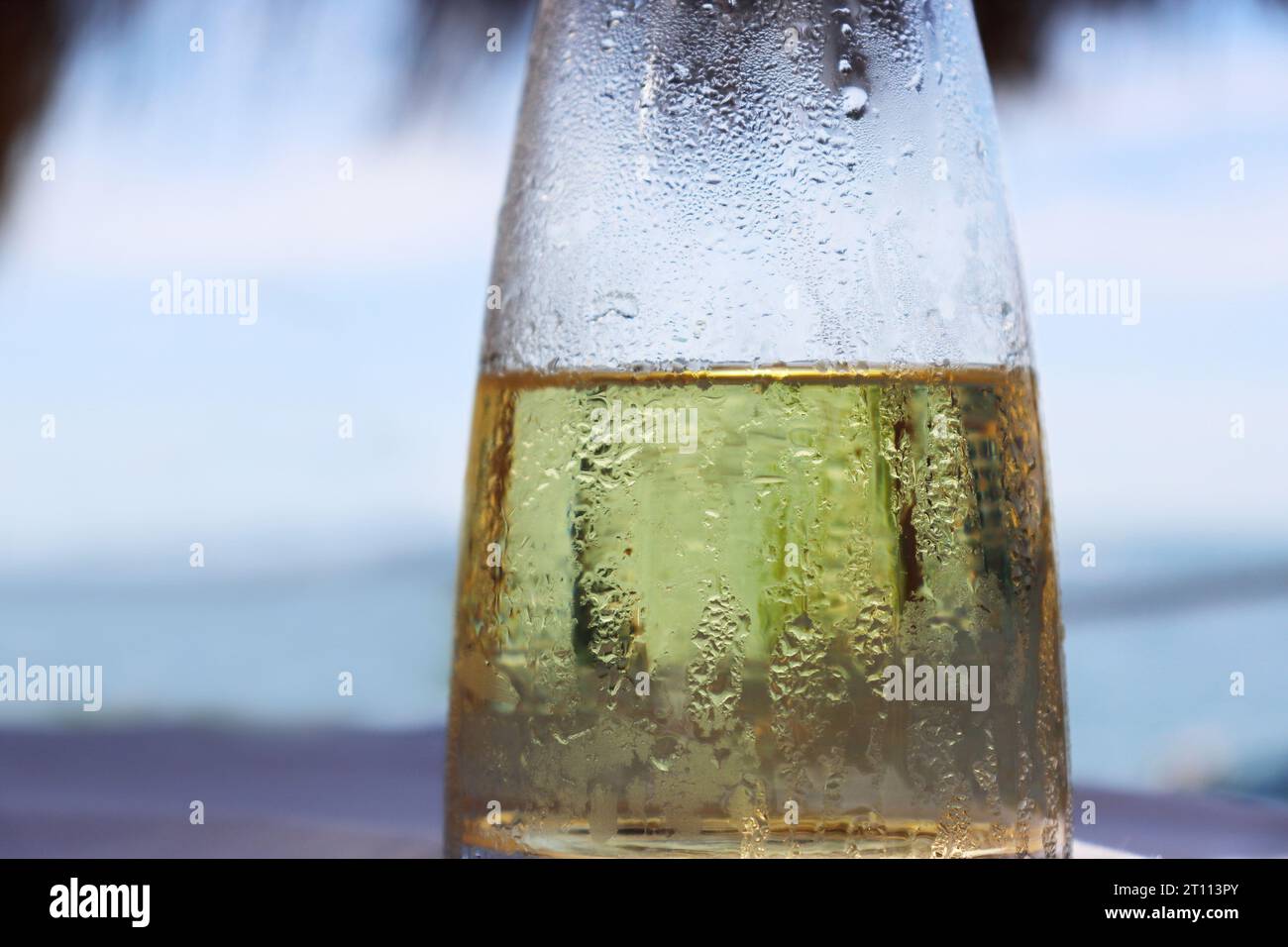Fresh fruit water in a glass pitcher on the table in the restaurant at the sea shore. Ice cold lemonade at the beach. Detail of the bottle. Drops of w Stock Photo