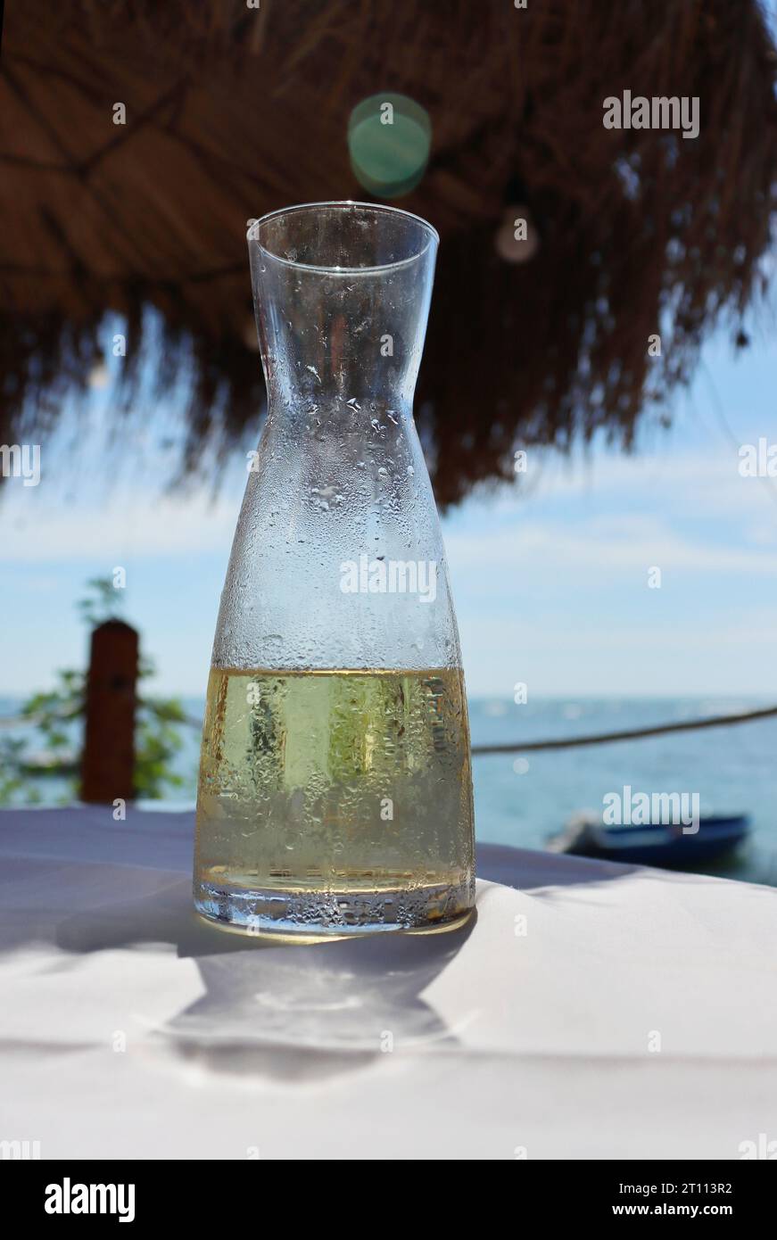 Fresh fruit water in a glass pitcher on the table in the restaurant at the sea shore. Ice cold lemonade at the beach. Detail of the bottle. Drops of w Stock Photo