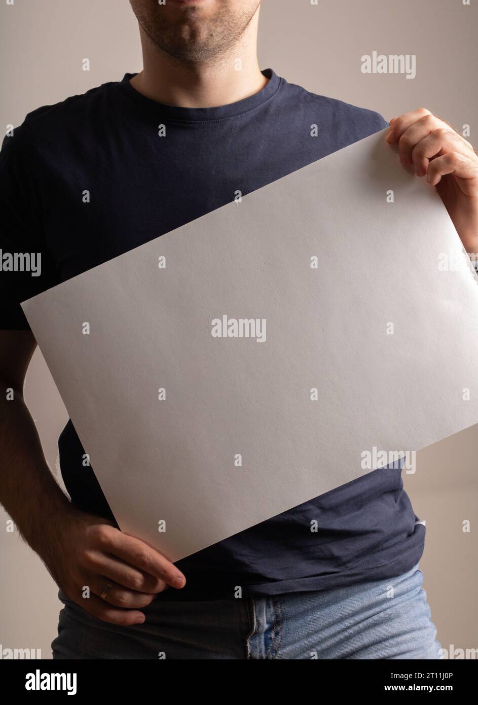 photo a man stands holding a blank white sheet of paper, showing empty space for information. The poster-like display awaits text, a canvas for convey Stock Photo