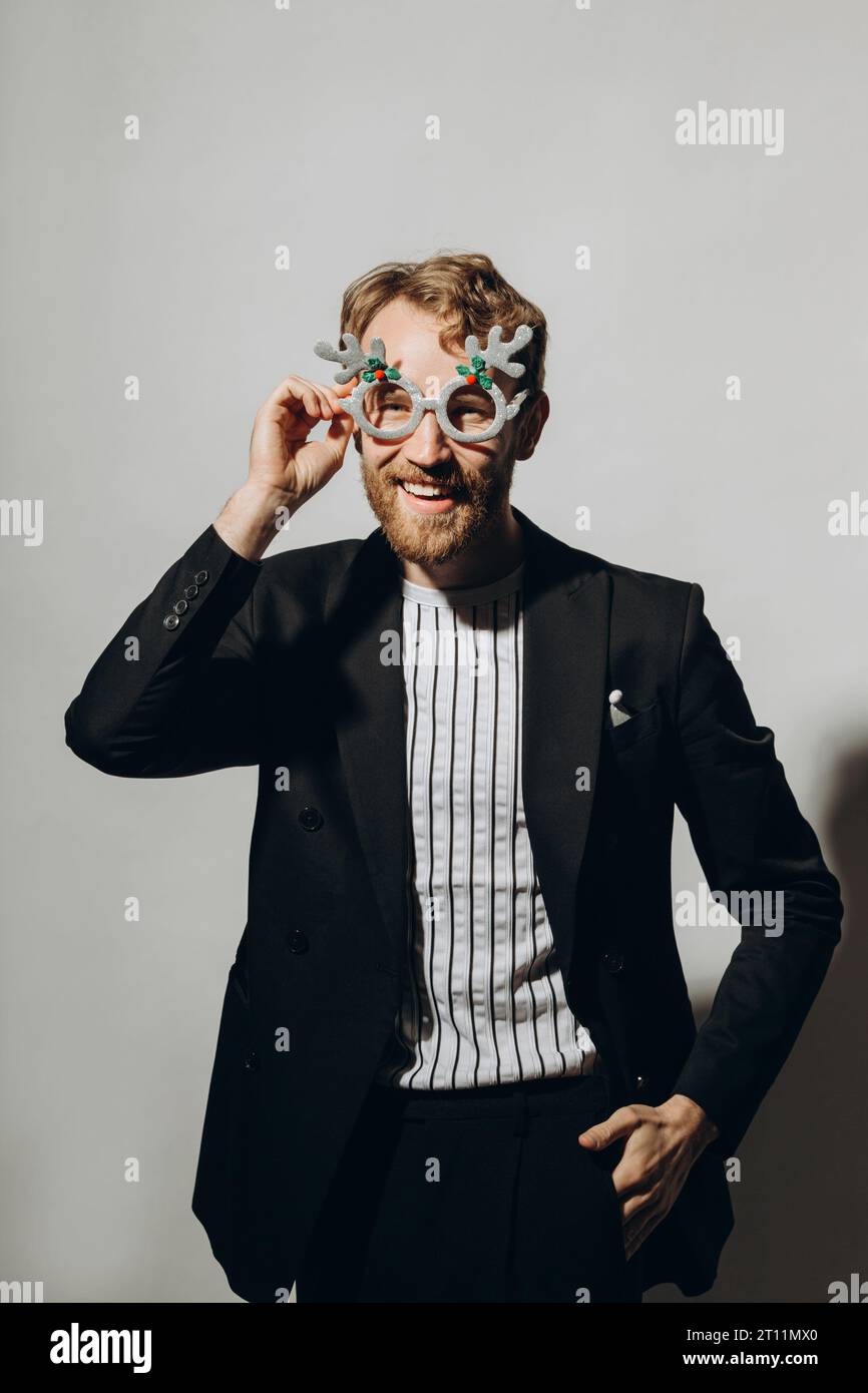 Young man in black jacket with party glasses on color background. Stock Photo