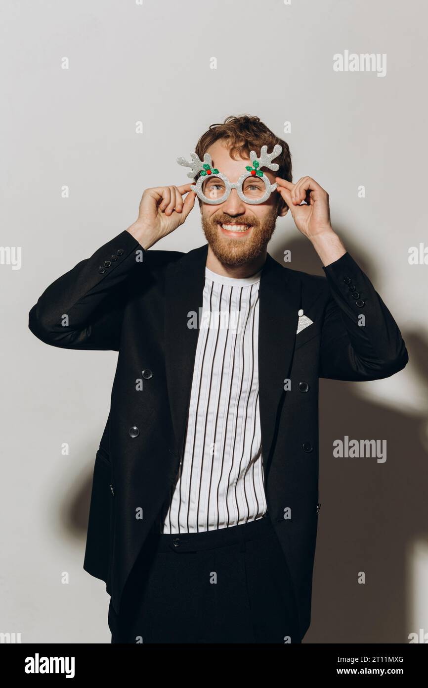 Young man in black jacket with party glasses on color background. Stock Photo