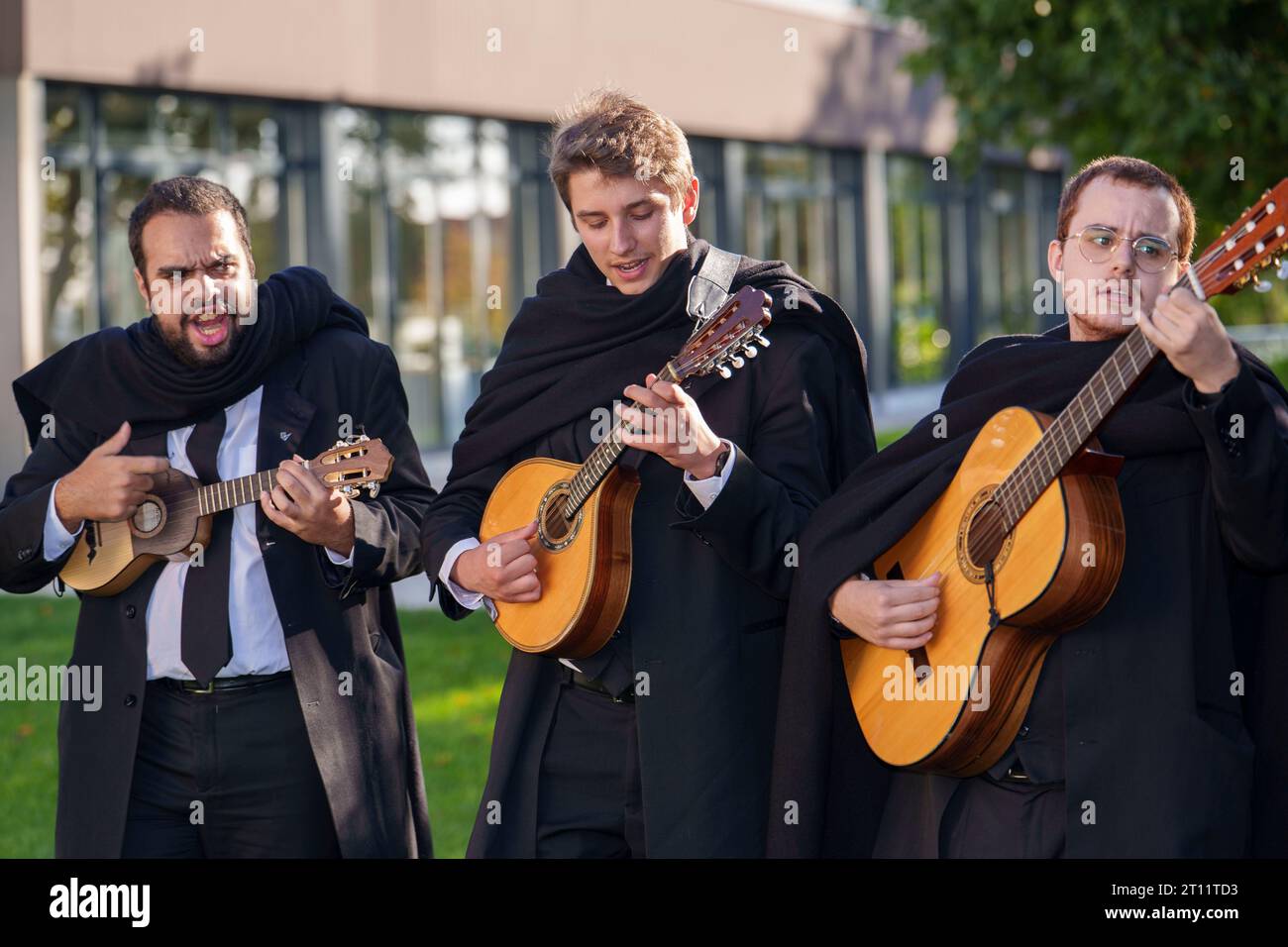 Students with traditional academic attire and black cape sing and play musical instruments as members of the Estudantina Universitária de Coimbra Stock Photo
