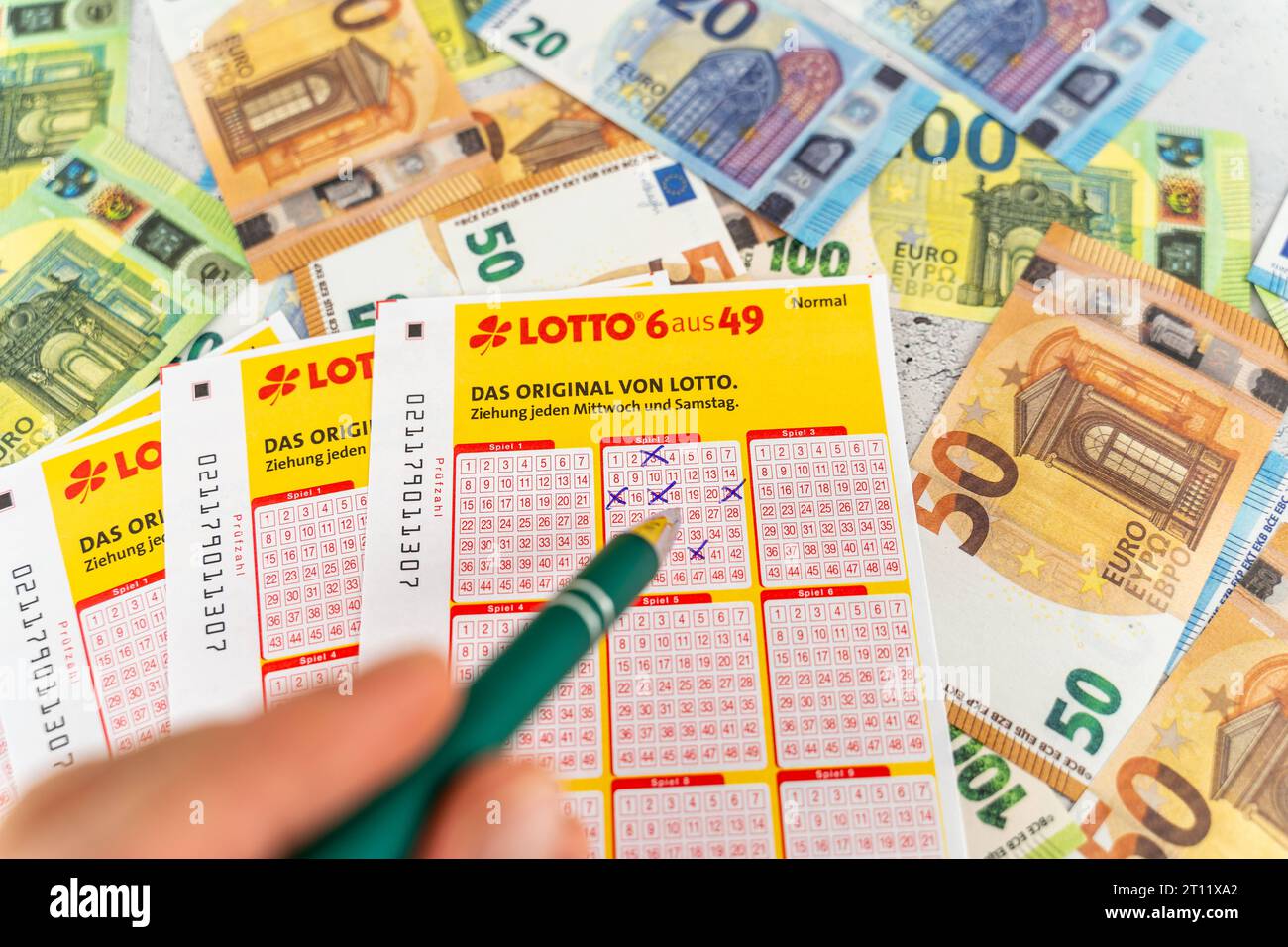 Augsburg, Bavaria, Germany. 10th Oct, 2023. Lotto 6 out of 49 tickets on Euro cash bills. Gambling lottery, hand fills in betting boxes with ballpoint pen *** Lotto 6 aus 49 Spielscheine auf Euro Bargeld Scheinen. Glücksspiel Lotterie, Hand füllt Tippfelder aus mit Kugelschreiber Credit: Imago/Alamy Live News Stock Photo