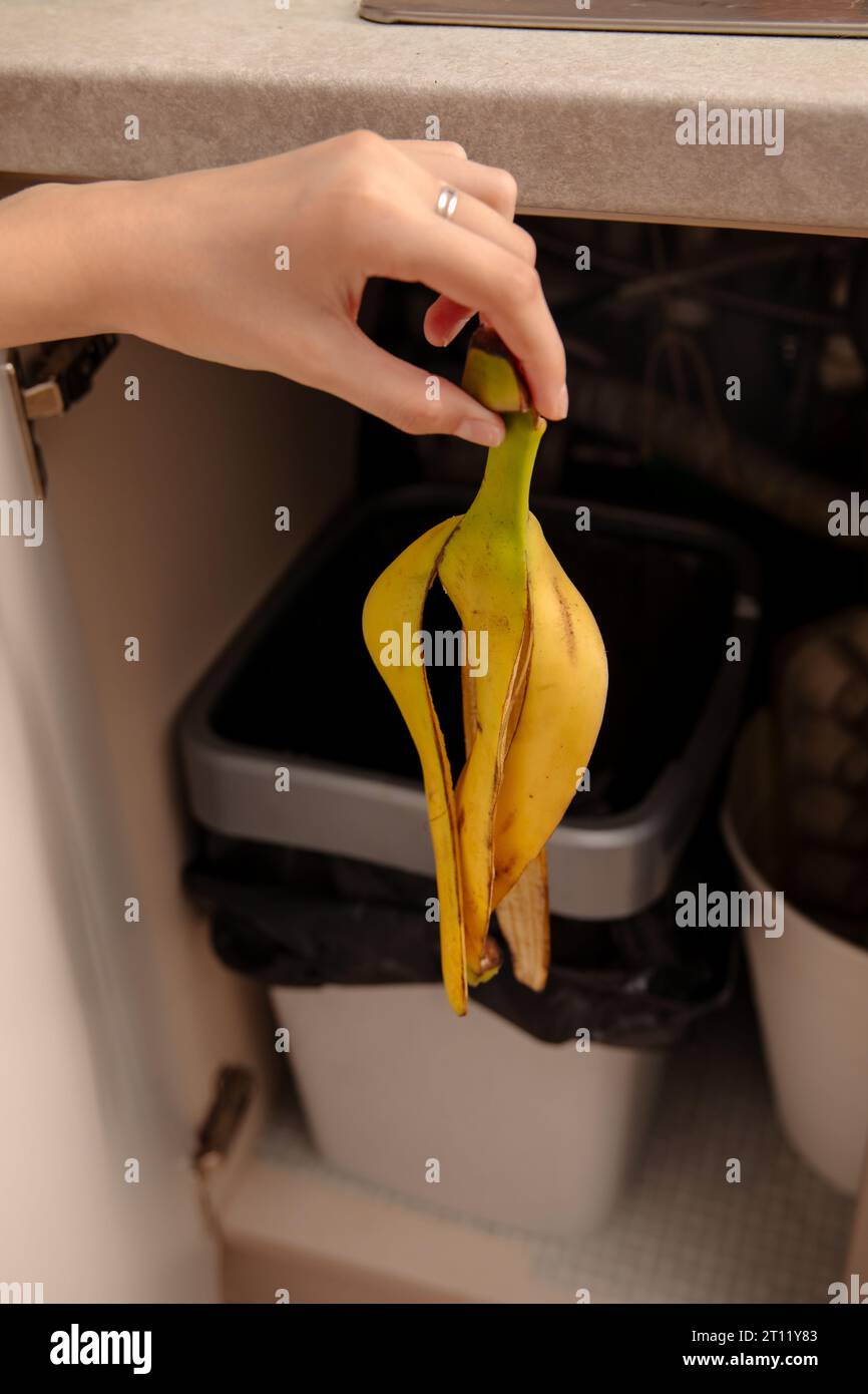Woman putting banana peel in a trash bin. Kitchen and home Stock Photo