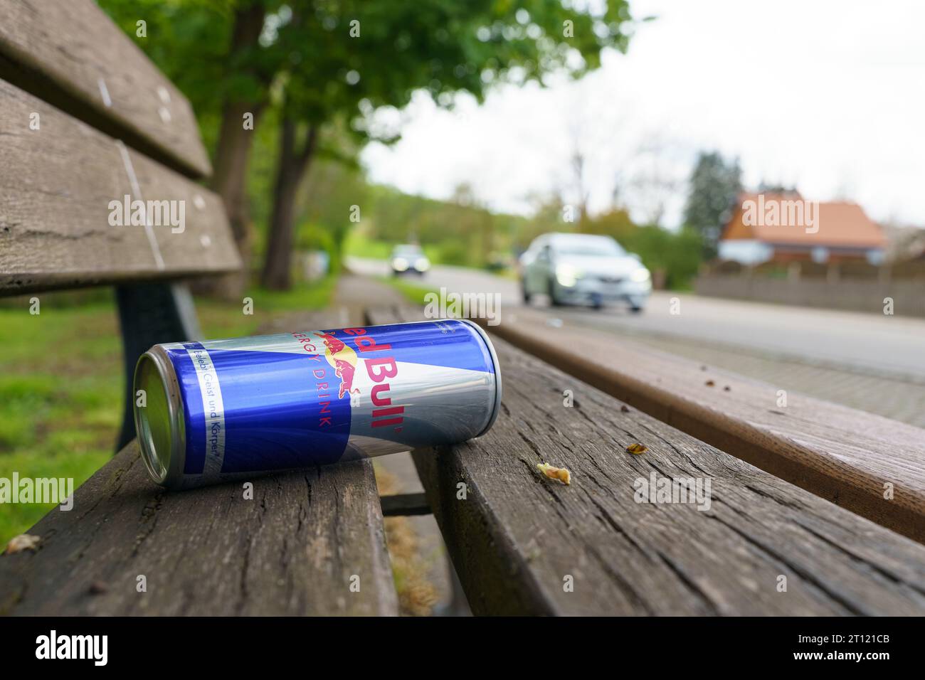 Weinberg, Germany - May 6, 2023: On a wooden bench lies an empty metal can of energy drink - Red Bull. In the blurry background, cars are driving alon Stock Photo