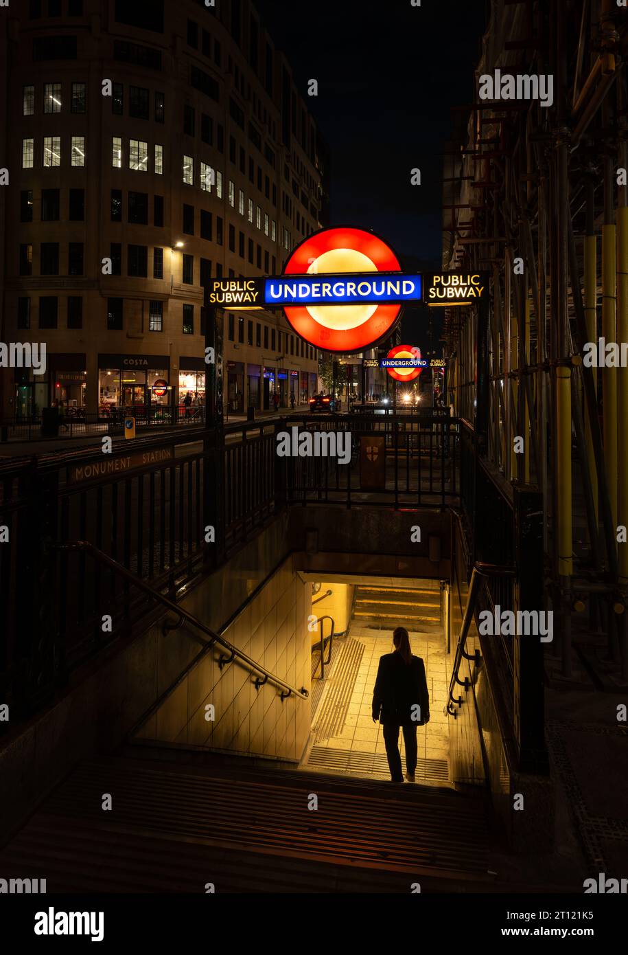 London, UK: Entrance to Monument tube station at night with illuminated London Underground sign and a person walking down the steps. Stock Photo