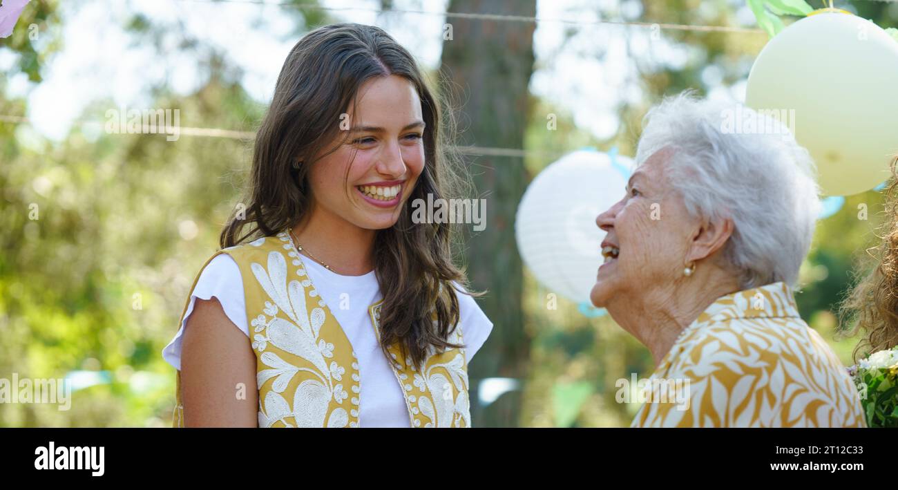 Mature granddaughter and grandmother reunite after a long time, talking. Family gathering at a garden party. Banner with copy space. Stock Photo