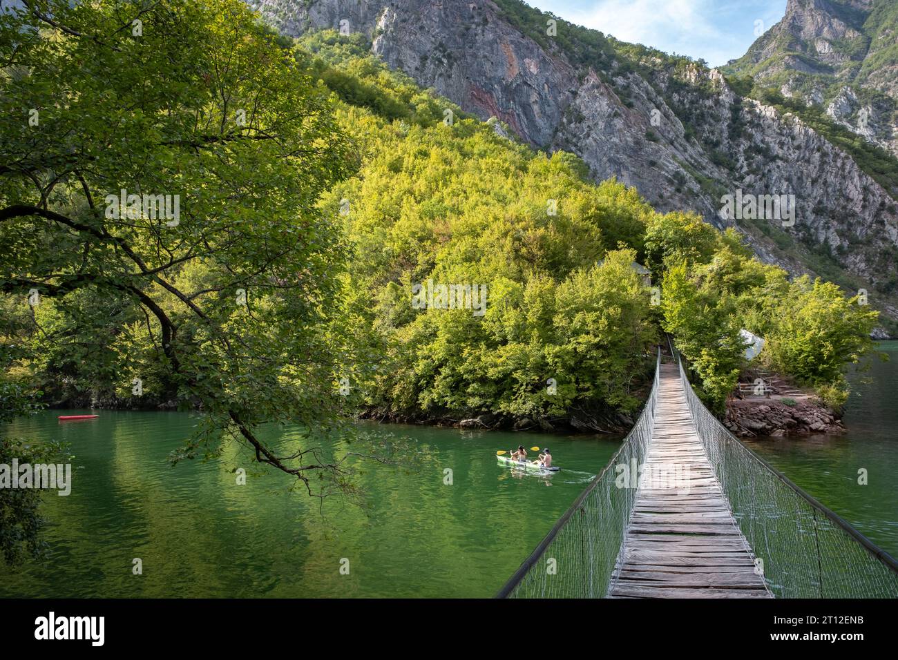 Two people in a kayak going under a wooden rope bridge at Lake Komani, Albania Stock Photo