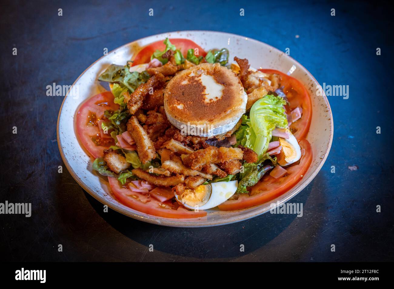 Salad with ham, cheese and chicken on a black background, on a white plate Stock Photo