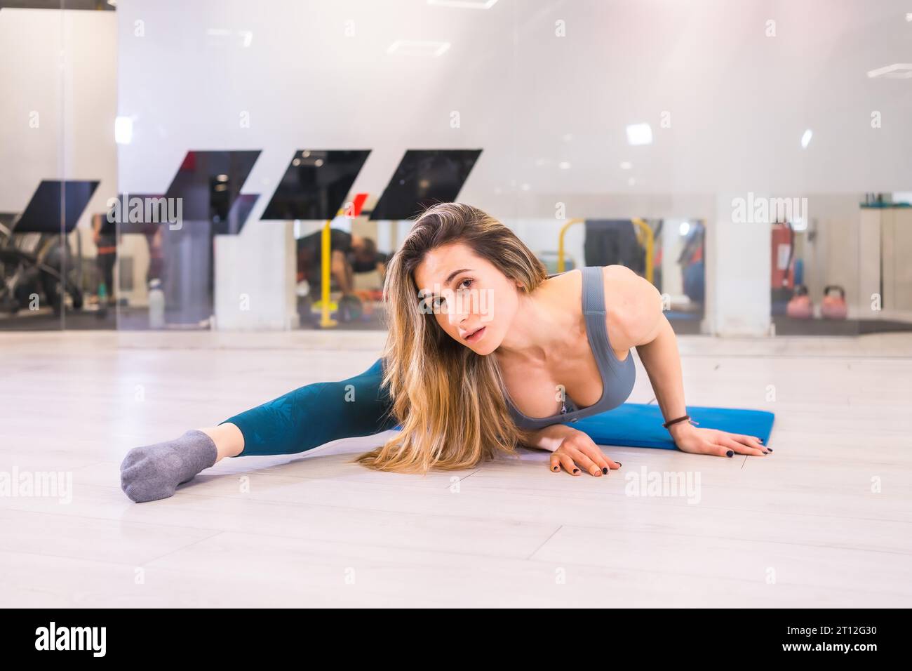 Lifestyle training in a gym, sport and health wellness. Pretty blonde girl of Caucasian ethnicity performing gymnast stretching Stock Photo