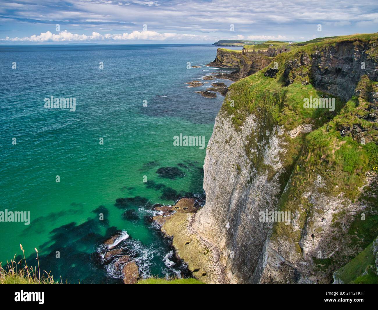 High coastal cliffs on the Antrim Coast, near Giant's Causeway, Northern Ireland. The ruins of Dunluce Castle appear in the background. Stock Photo