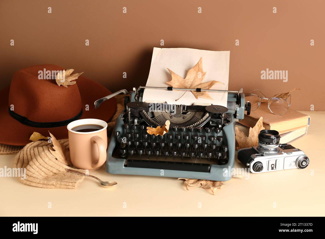 https://c8.alamy.com/comp/2T1337D/vintage-typewriter-hat-books-photo-camera-cup-of-coffee-eyeglasses-and-autumn-leaves-on-brown-background-2T1337D.jpg