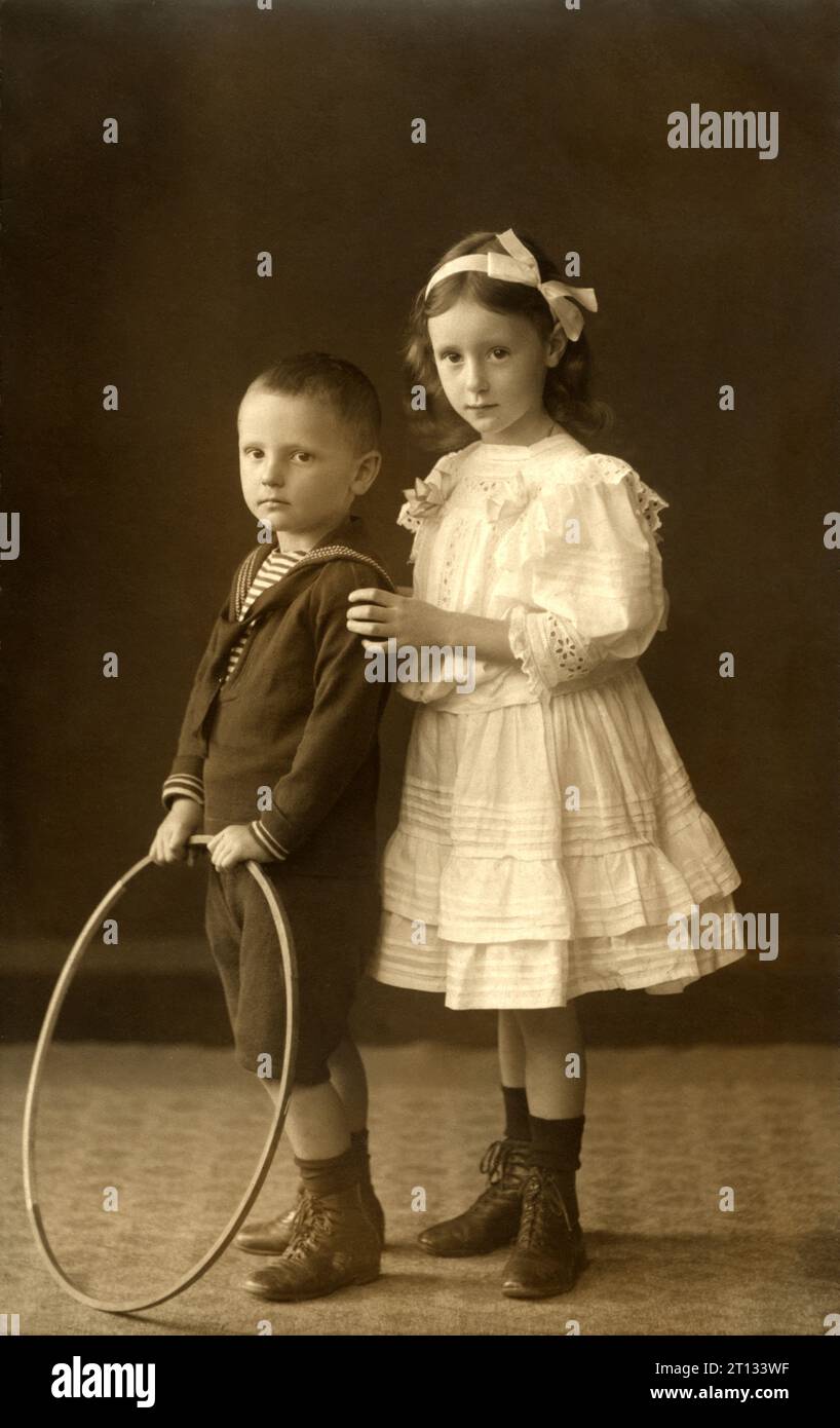 1911 , september , DETMOLD , GERMANY : Two children , brother  and sister . The boy named Wilhelm Heinrich and young girl named Gertrud . Photo by Reckmam , Detmold  . - North Rhine-Westphalia - FAMILY - FAMIGLIA - DUE - TWO FRATELLI - FRATELLO - BROTHER - SORELLE - SORELLA - GERMANIA  - FOTO STORICHE - HISTORY PHOTOS - BAMBINO - BAMBINI - BAMBINA - BAMBINE - CHILDREN - CHILD - BABY - CHILDHOOD - INFANZIA - BABY -  ANNI DIECI - '10 - 10's - vestito alla marinara - marinaretto - marina - sailor dress - cerchio - cerchione - TOY - GIOCO - GIOCATTOLO - GIOCO - BIG RIM - FASHION - MODA INFANTILE - Stock Photo