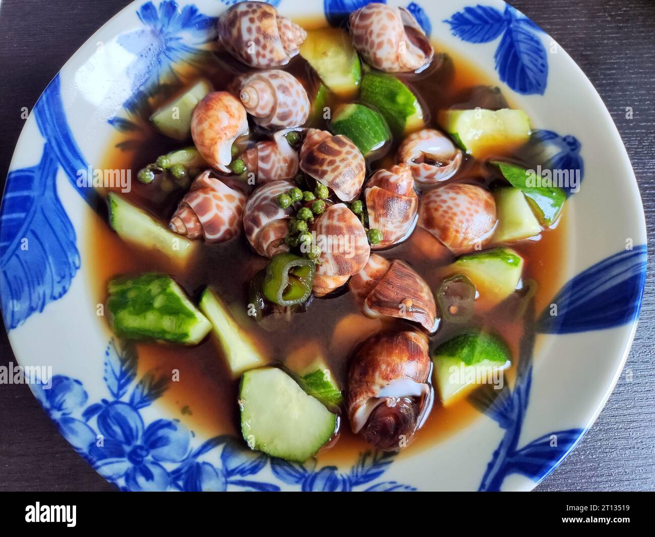 grilled Babylonia lutosa with green cucumber in the soy soup in the blue plate Stock Photo
