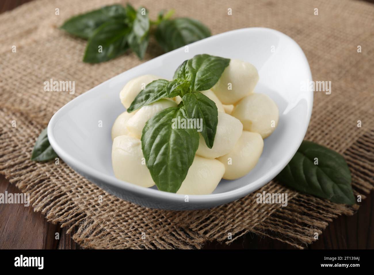 Tasty mozarella balls and basil leaves in bowl on table, closeup Stock Photo