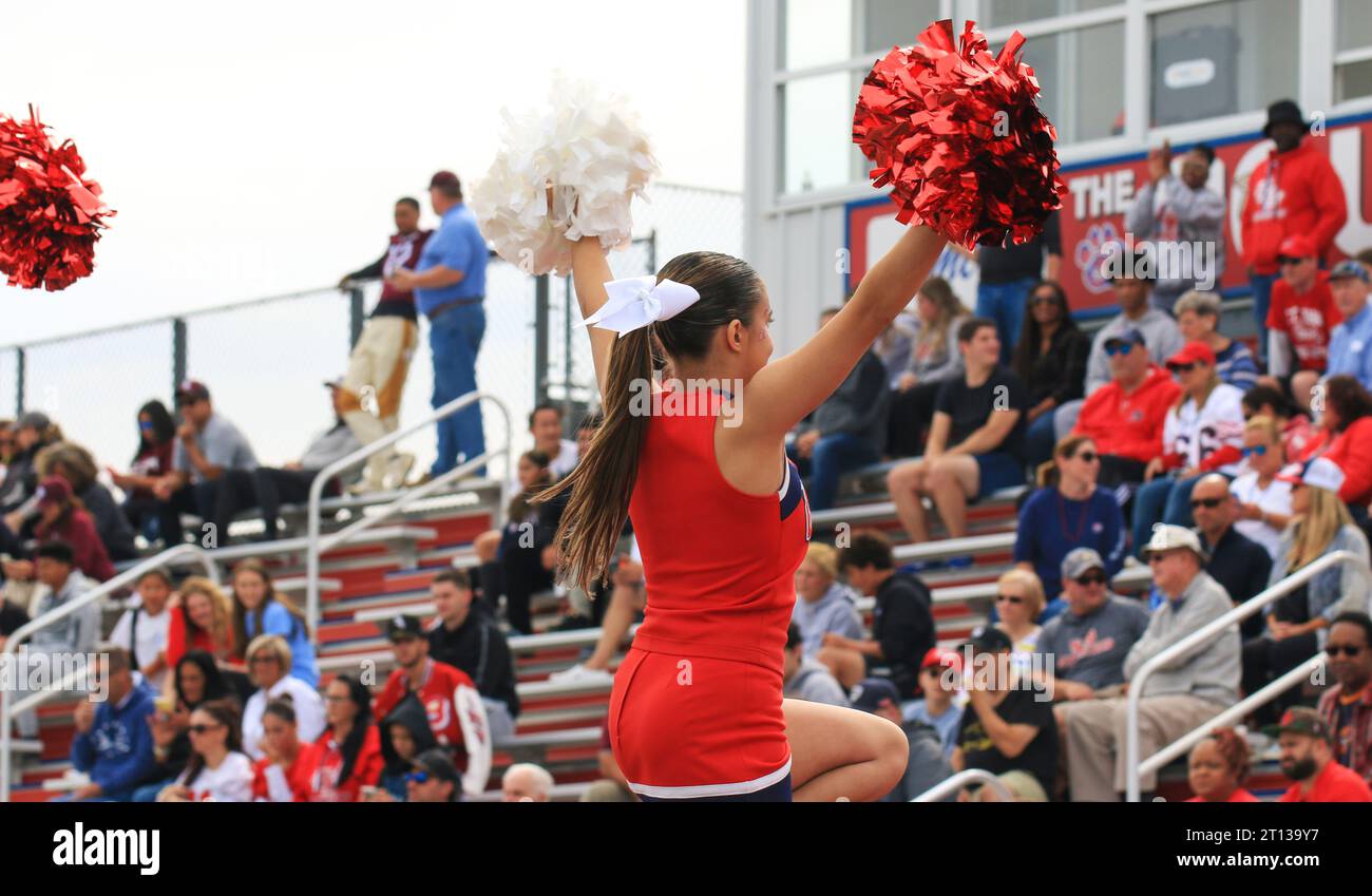 West Islip, New York, USA - 16 September 2023: Rear view of a high school cheerleader being held in the air waving to the crowd in the stands with her Stock Photo