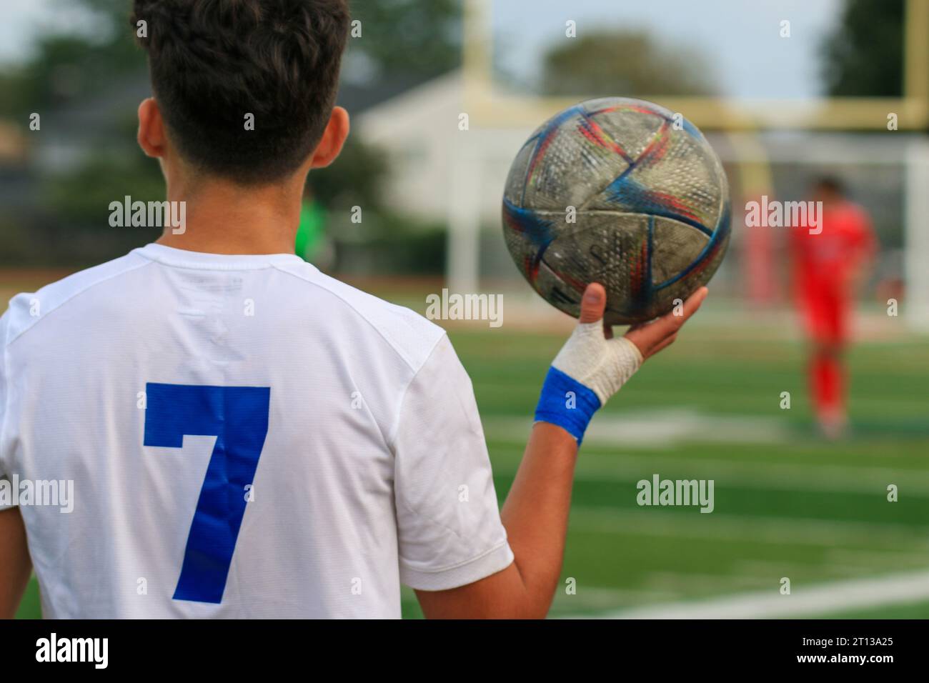 Rear view of a male high school soccer player holding up the ball with one hand during a match. Stock Photo