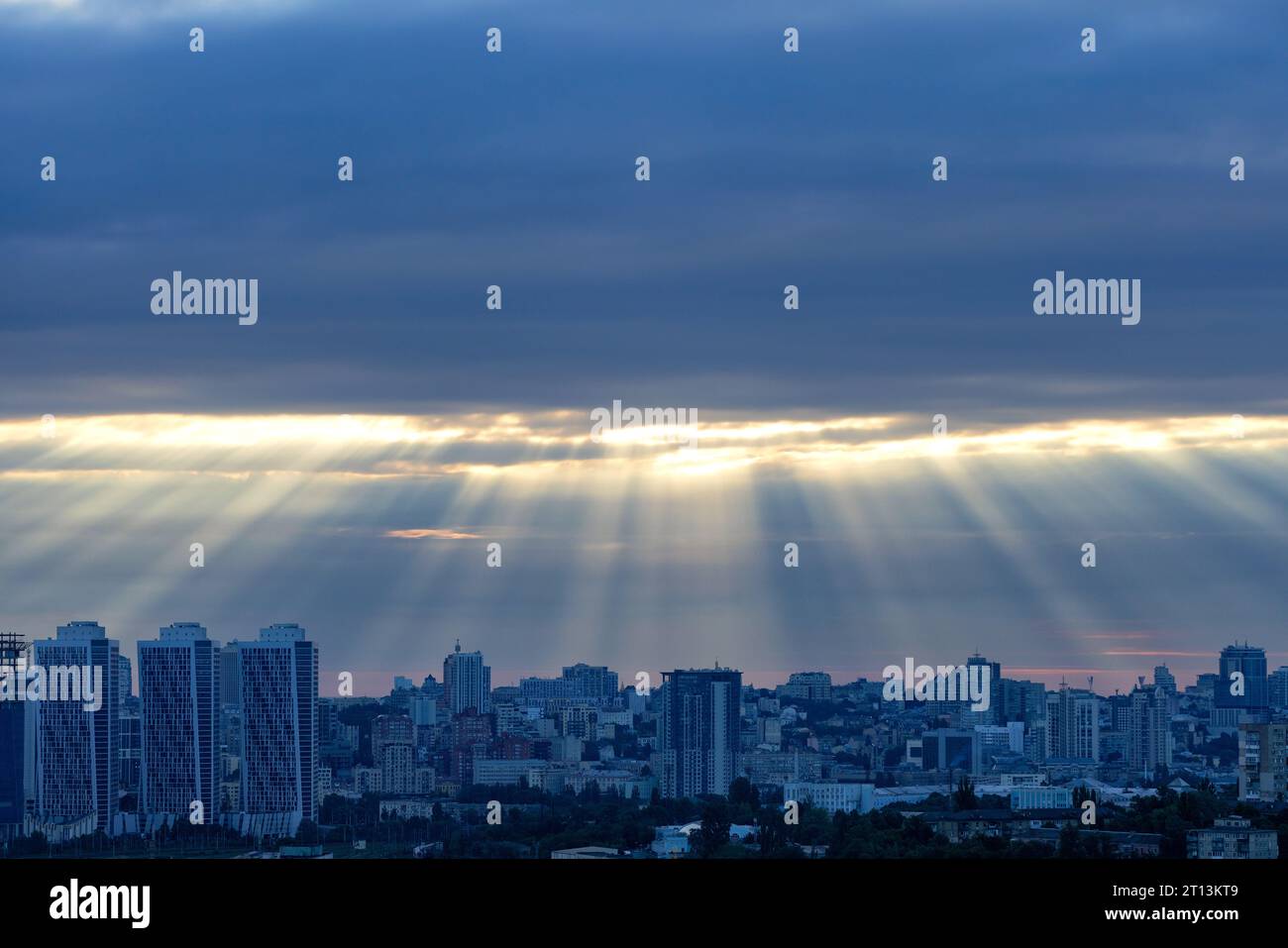 The sun's rays at dawn in the blue break through the thick clouds over the sleeping city. Shining light in a dramatic morning sky. Stock Photo