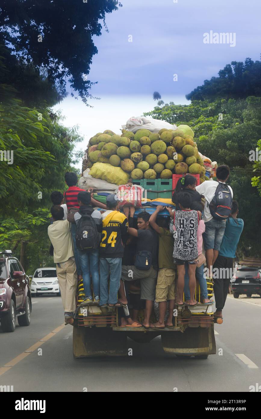 Cagayan de Oro, Philippines: people hang on to the back of a moving jeepney, top loaded with fruits, sacks of vegetables, crates of beer. Public transport. Stock Photo
