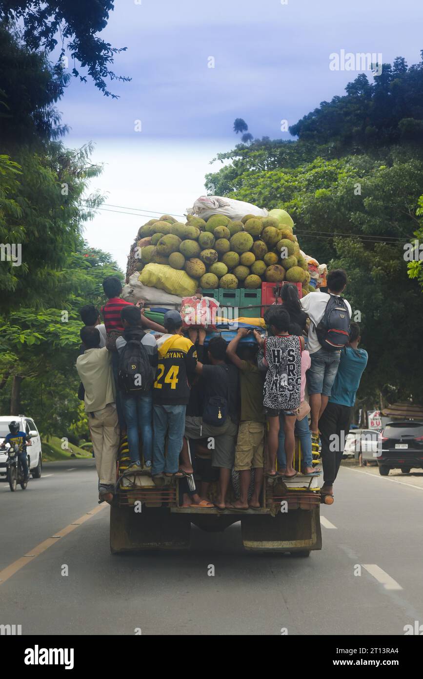 Cagayan de Oro, Philippines: people hang on to the back of a moving jeepney, top loaded with fruits, sacks of vegetables, and crates of beer. Public transport. Stock Photo