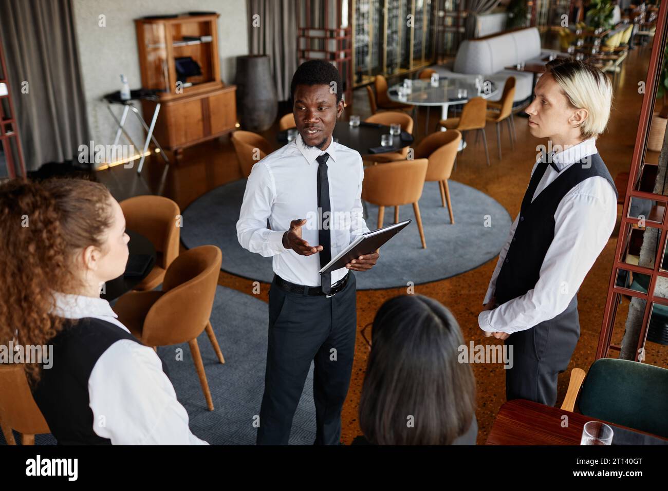 High angle portrait of restaurant manager talking to servers wearing