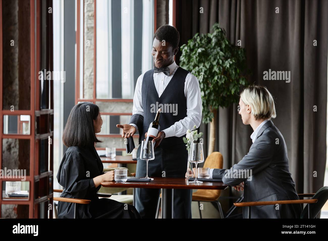 Portrait of Black young man as smiling waiter taking orders from couple ...