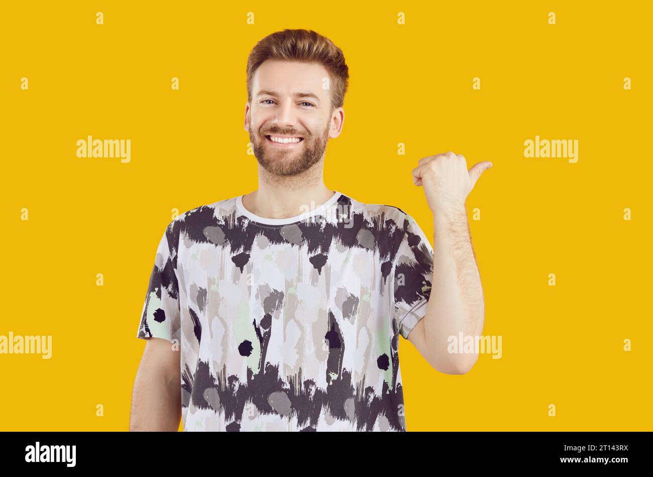Portrait of a happy man in a T shirt standing pointing his thumb to the side and smiling Stock Photo