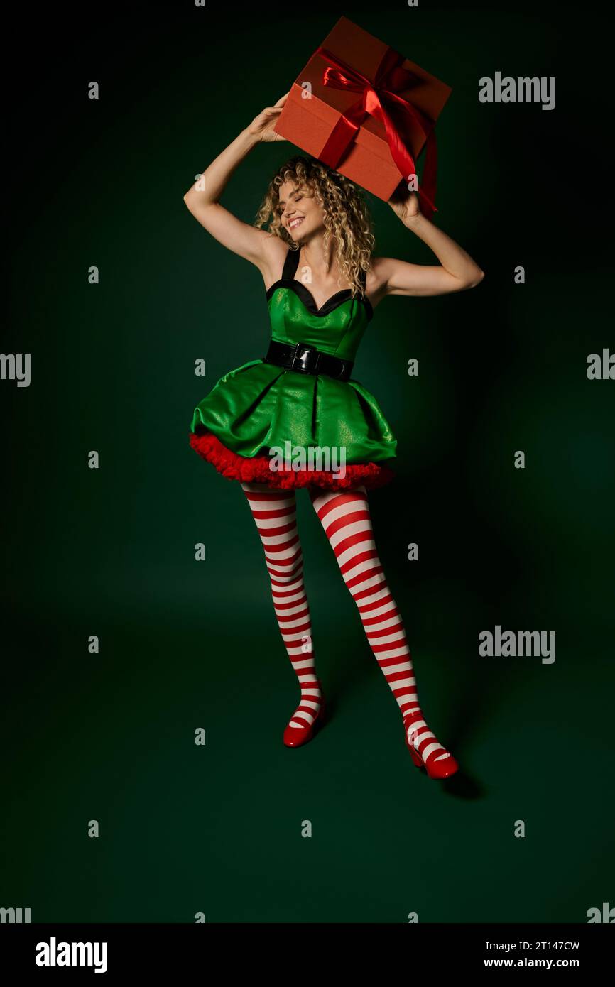smiley new year elf in festive green dress holding present above her head  and looking away Stock Photo - Alamy