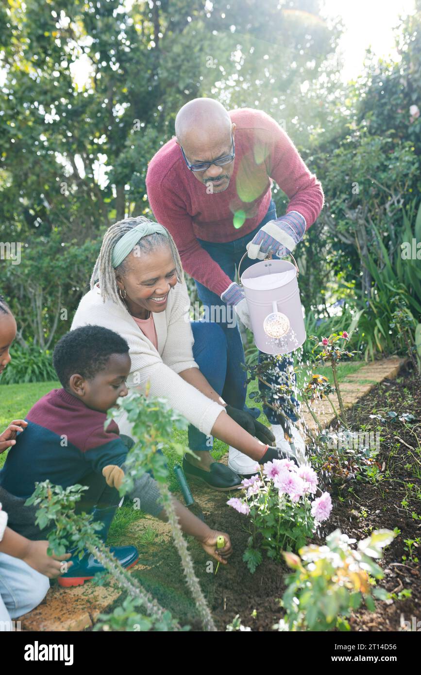Happy african american grandparents and grandchildren watering plants
