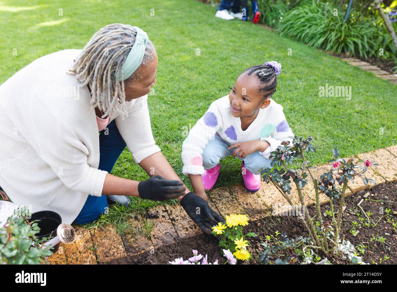 Happy african american grandmother and granddaughter taking care of plants in sunny garden Stock Photo