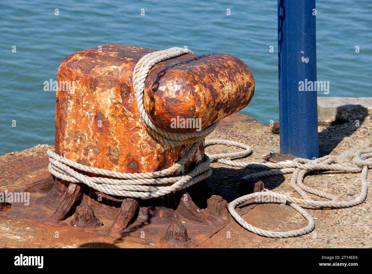 Large bollard with rope round it and part of blue metal post at end of concrete jetty, Whitstable, Kent Stock Photo