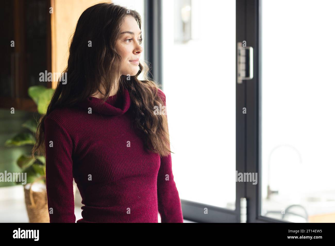 Thoughtful caucasian woman looking through window in kitchen at home Stock Photo