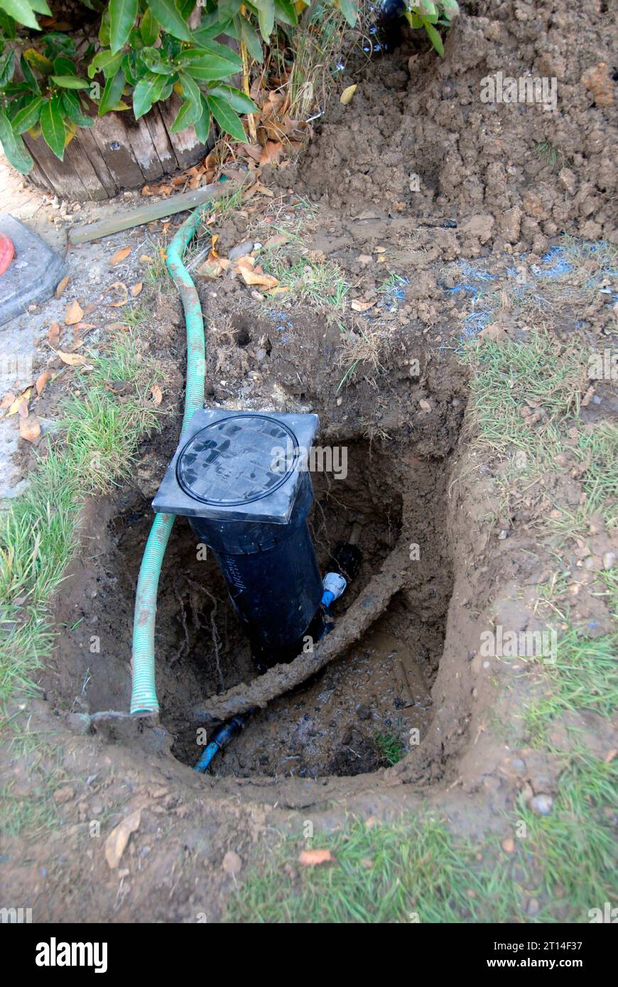 Hole dug in grass area to replace leaking water meter, with other service pipes exposed Stock Photo