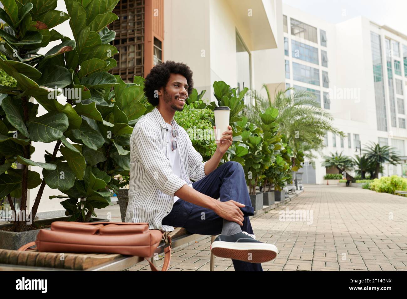 Happy Black man sitting outdoors, drinking coffee and enjoying good weather Stock Photo