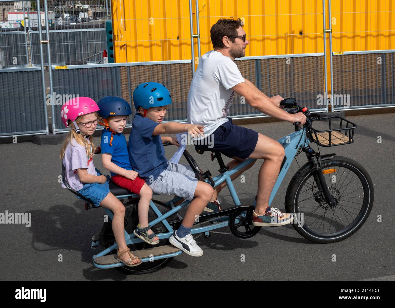 A boy points as a father rides an electric bicycle carrying three young children on the rear in Paris, France. The bike is a Decathlon ELOPS BTWIN ele Stock Photo