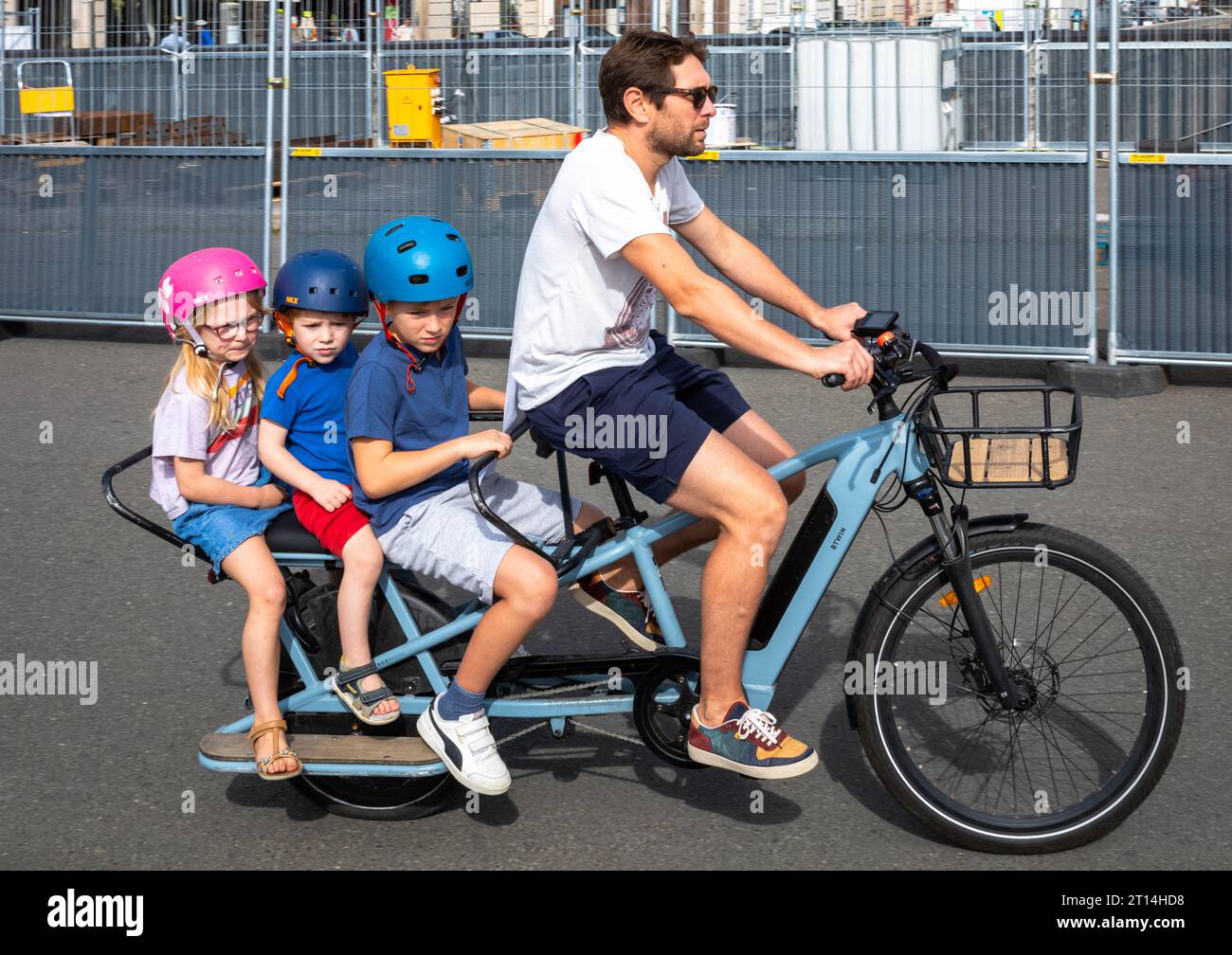A father rides an electric bicycle carrying three young children on the rear in Paris, France. The bike is a Decathlon ELOPS BTWIN electric rear loadi Stock Photo
