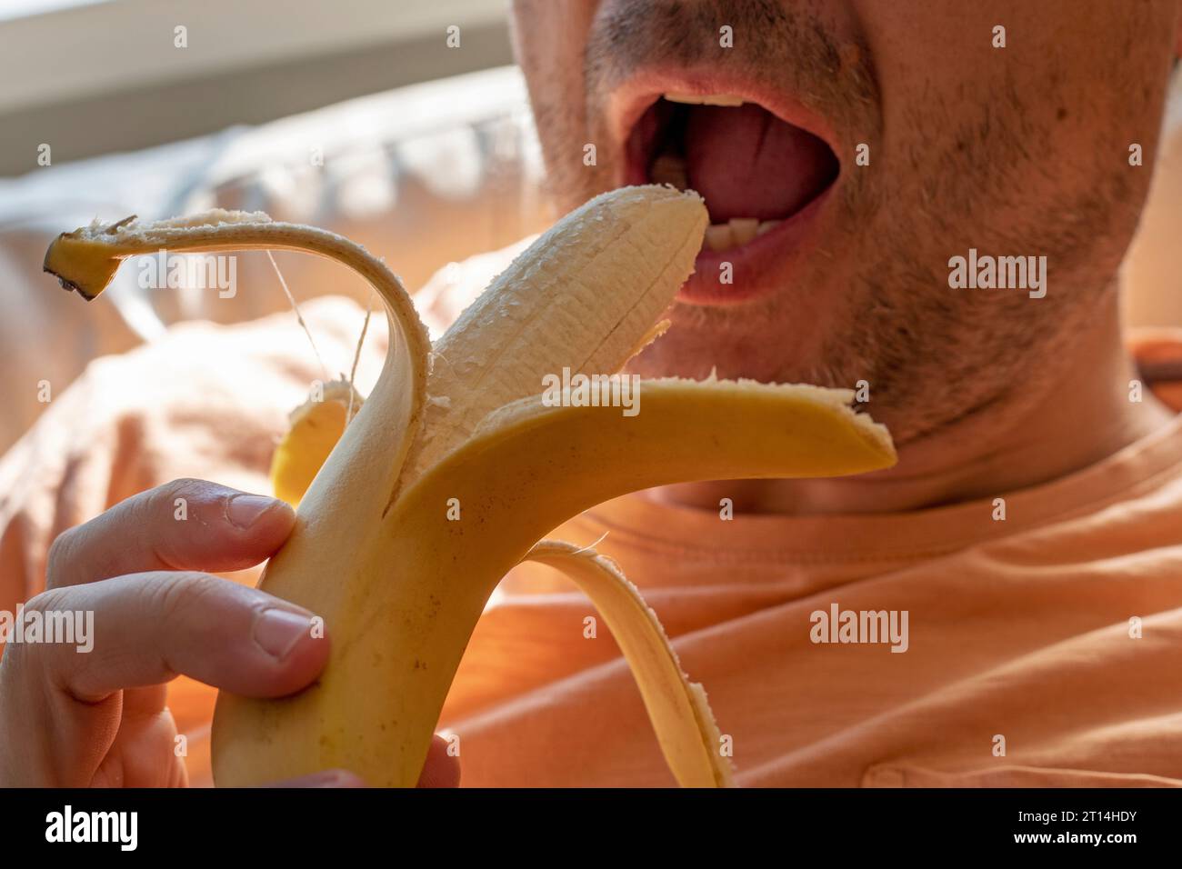 man holds a peeled banana before eating it with his mouth open Stock Photo