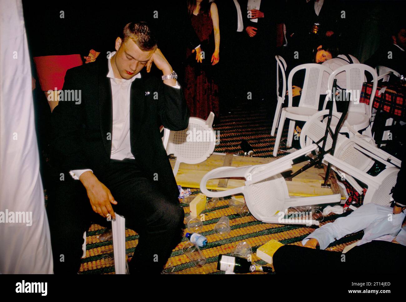Alcohol abuse, drinking culture male students 1990s UK. A male tired and drunk student, exhausted and asleep at the end of the year annual summer May Ball. Another drunk student lies dead to the world amongst the over turned plastic chairs and tables. Cirencester Royal Agricultural College, Cirencester Gloucestershire, England, circa May 1995. HOMER SYKES Stock Photo